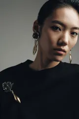 Maxi pendientes colgantes con diseño de flor en relieve en tonos blanco y negro, unidas a una pieza metálica dorada con forma de jarrón alargado.