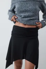 Minifalda negra de tiro medio con detalle de frunces en la cintura y bajo asimétrico con caída fluida.