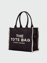 Bolso tote de lona color beige con estampado frontal en negro que dice 'THE TOTE BAG MARC JACOBS'. Presenta bordes laterales en color negro con detalles de texto y doble asa superior.