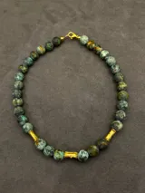 Collar Ound modelo Guayabo, elaborado con cuentas esféricas de piedra en tonos verdosos y marrones, intercaladas con separadores cilíndricos dorados. Cierre de mosquetón dorado.