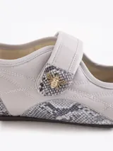 Mary Jane de nylon liviano color gris, combinada con recortes en cuero vacuno y descarne con estampado animal print tipo serpiente en la puntera y el talón. Cuenta con una tira con cierre de velcro en el empeine decorada con un aplique metálico en forma de abeja.