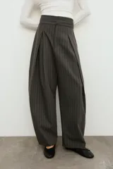 Pantalón balloon de tiro alto y diseño abuchonado, en color marrón oscuro con sutiles rayas verticales. Cuenta con pinzas y pliegues pronunciados en el delantero.