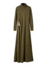 Vestido largo de punto en color verde oliva, con cuello alto y manga larga. Presenta un diseño ajustado en la parte superior que se extiende hacia una falda recta, con un detalle metálico decorativo en el lateral de la cintura.