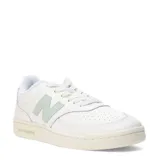 Championes urbanos New Balance, modelo Pop N Pack Leather, de color blanco con detalles en verde pastel en el logo lateral y la suela. Presentan una silueta clásica de corte bajo con perforaciones en la puntera y cierre de cordones.