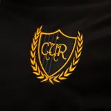 Camiseta de fútbol Puma del Club Atlético Peñarol, edición aniversario manga larga. Diseño con mitad derecha a rayas verticales amarillas y negras, y mitad izquierda negra con escudo retro "CUR" en dorado. Cuenta con cuello tipo polo negro con detalles amarillos y sponsors impresos en el frente y mangas.