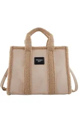 Cartera tipo tote de Las Oreiro, confeccionada en gamuza sintética color beige con detalles de corderito en los bordes y manijas. Incluye un parche frontal con el logo de la marca y correa ajustable extraíble.