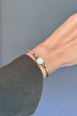 Pulsera rígida de bronce con diseño minimalista, que presenta un engaste central circular con incrustación de nácar.