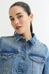 Chaqueta de jean celeste con apliques de strass en cuello y hombros, corte clásico, mangas largas y bolsillos frontales.