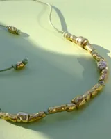 Collar artesanal compuesto por piezas metálicas irregulares con acabado dorado, ensartadas en un cordón de hilo de algodón natural. Presenta un sistema de nudo corredizo para ajustar el largo.