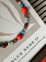Collar corto de cuentas multicolor que combina cuentas esféricas de piedra jaspe dálmata, cuentas turquesas, cuentas naranjas brillantes, cuentas marrones y abalorios translúcidos, con cadena de ajuste y cierre de mosquetón plateado.