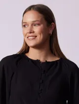 Blusa de gasa blanca con estampado de hojas en azul marino, cuello a la base con escote en V y botones, y mangas cortas abullonadas.