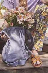 Bolso tipo bucket color celeste con textura simil cuero de cocodrilo, cierre con cordón ajustable, correa de hombro ajustable y asa de mano.