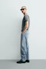Jeans de denim de algodón en color negro con efecto lavado, corte amplio y silueta curva tipo barrel fit con pinzas en las rodillas. Presenta diseño clásico de cinco bolsillos y cierre frontal con cremallera y botón metálico.