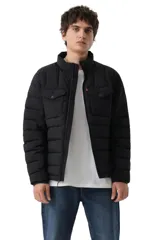 Campera puffer negra con diseño acolchado horizontal, cierre frontal completo y cuello alto. Cuenta con dos bolsillos frontales con solapa y cierre de botón a presión, y el distintivo logo de la marca en una etiqueta roja lateral.