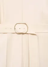 Mono largo de corte recto y color beige, con cuello en pico, mangas cortas y cinturón incorporado con hebilla metálica. Cuenta con cierre de cremallera en la parte posterior.