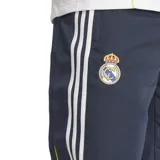 Pantalón deportivo azul marino Adidas UBP Real Madrid, con cintura elástica, cordón de ajuste y bolsillos laterales con cierre. Presenta el escudo del Real Madrid bordado en la pierna izquierda y las tres líneas características de Adidas en blanco a lo largo de la pierna.