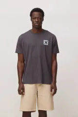 Remera de manga corta color gris oscuro, con cuello redondo y estampa pequeña en el pecho que consiste en una cruz negra sobre un cuadrado celeste.
