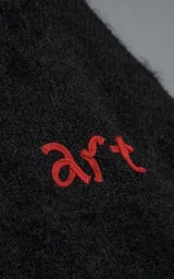 Sweater de punto negro con textura suave, cuello redondo y diseño oversize. Presenta un bordado frontal con la frase 'art SUPPORT' en letras rojas y blancas, y un pequeño detalle de tijeras bordado en la nuca.