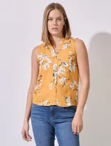 Blusa amarilla sin mangas de satén estampado con flores blancas. Tiene cuello a la base y escote en V.