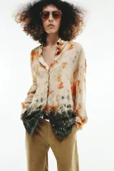 Camisa de manga larga con cuello solapa y cierre frontal con botones, con diseño tie-dye en tonos beige, naranja y verde oscuro en el sector inferior.