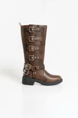 Borcegos de caña alta confeccionados en cuero sintético con acabado envejecido. Presentan múltiples hebillas metálicas decorativas a lo largo del lateral y una correa ajustable con hebilla doble en la zona del tobillo. Cuentan con suela de goma negra con plataforma y cierre lateral.