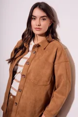 Sobrecamisa negra de estilo shacket, confeccionada en tejido de gamuza sintética. Presenta cuello camisero, cierre frontal de botones y dos bolsillos de parche con solapa en el pecho. El calce es oversize y las mangas son largas.