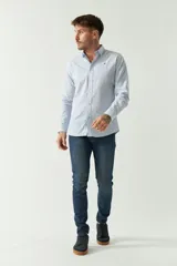 Camisa de hombre de corte slim, manga larga, con cuello clásico y cierre frontal con botones. Presenta un diseño a rayas verticales finas en tonos claros y un pequeño logo bordado en el pecho.