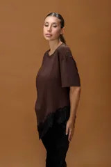 Remera de color marrón con cuello redondo y mangas cortas. Presenta un diseño asimétrico en el ruedo con un delicado detalle de encaje negro aplicado.