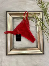 Pack de tres tangas de encaje con diseño floral, breteles regulables y laterales finos. El conjunto incluye una tanga rosa claro, una tanga color tostado con bordes grises y una tanga roja.