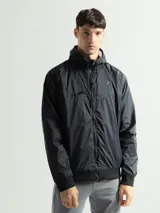 Campera deportiva negra de nylon impermeable con capucha y cierre frontal. Presenta puños y cintura elásticos de tejido acanalado. Tiene un pequeño logo blanco en el pecho.