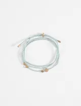 Pulsera de cordón trenzado color celeste con hilo plateado, con dijes metálicos dorados en forma de corazón, trébol de cuatro hojas y cruz.