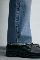Jeans de mezclilla rígida de algodón, color azul claro con efecto lavado y ligero desgaste. De tiro medio, corte recto desde la cadera hasta la rodilla y ligeramente acampanado en el bajo (bootcut). Cierre frontal con botonadura y cinco bolsillos.