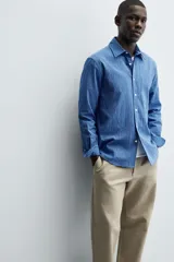 Camisa de corte regular fit confeccionada en tejido de algodón con textura. Presenta cuello solapa, cierre frontal de botones, manga larga con puños abotonados y un bolsillo plastrón en el pecho.