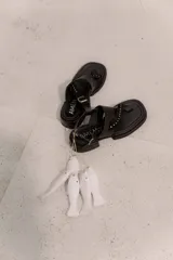 Sandalia de cuero vacuno color negro, con diseño de tiras cruzadas, detalle de tachas metálicas, ajuste con hebilla en el tobillo y suela con tacón bajo.