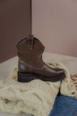 Bota estilo western de caña media, confeccionada en una combinación de cuero texturizado en la parte inferior y gamuza en la caña. Presenta costuras decorativas en contraste y suela de goma robusta con plataforma.