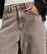 Pantalón de jean con corte barrel, de cintura alta y diseño de piernas anchas con volumen redondeado. Presenta bolsillos funcionales, trabillas para cinturón y cierre frontal con botón y cremallera.