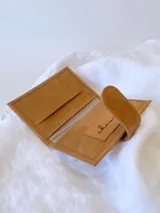 Tarjetero plateado de cuero con broche a presión. Tiene espacio para 4 tarjetas y billetes, y un bolsillo externo.