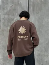 Buzo marrón con logo "Osten" y diseño gráfico de sol en color beige. Corte oversize, cuello redondo y mangas largas.