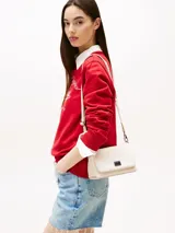 Cartera compacta Tommy Jeans de color blanco marfil con acabado liso, cierre de solapa magnética y detalle de parche metálico con logo en la parte delantera. Cuenta con una correa tejida ajustable y extraíble, compartimento principal y bolsillo interior con cremallera.