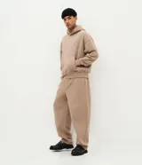 Pantalón baggy masculino de corte holgado, color beige, confeccionado en algodón con felpa. Posee cintura elástica con cordón ajustable, bolsillos delanteros y bajo con regulador por elástico.