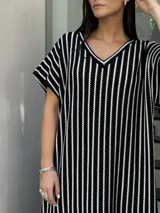 Vestido largo de tejido de punto con diseño de rayas verticales en blanco y negro. Presenta escote en V, mangas cortas y tajos laterales en el ruedo para mayor movimiento.