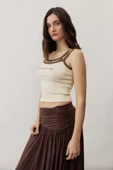 Musculosa de tejido rib color beige con detalles en marrón oscuro en el escote y doble tirante fino. Presenta un pequeño texto estampado en el pecho.