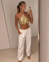 Top halter dorado con diseño de lentejuelas circulares colgantes y tiras finas ajustables al cuello y la espalda.