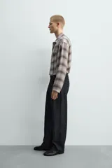 Camisa relaxed fit de manga larga con cuello solapa, confeccionada en tejido con mezcla de viscosa. Presenta un bolsillo plastrón en el pecho, bajo con aberturas laterales y cierre frontal de botonadura. El diseño es a cuadros en tonos beige y marrón.