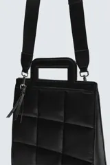 Bolso tipo shopper de diseño acolchado con patrón de cuadros, confeccionado en material sintético negro. Presenta asas de mano integradas en la estructura superior y un detalle de borla colgante con herraje metálico.