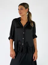 Camisa de satén color negro con cuello camisero, cierre frontal de botones y detalle de encaje negro en el borde inferior.