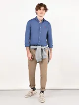 Camisa azul de hombre confeccionada en 100% algodón twill, tintada en prenda. Cuenta con corte regular fit, cuello button-down, cierre frontal de botones, manga larga con puño simple y pequeño logo rojo bordado en el pecho.