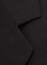 Blazer de corte sastre y diseño cruzado, con cierre de botones frontales, solapas clásicas y bolsillos laterales con solapa. Presenta una estructura entallada y hombros definidos.