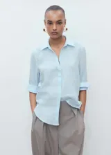 Camisa de lino celeste, de corte recto, con cuello camisero, cierre frontal de botones y mangas largas con puños abotonados.