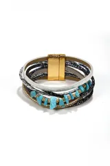 Brazalete multicapa con cierre magnético dorado, compuesto por tiras de cuero sintético, cordones brillantes y piedras naturales en color turquesa.
